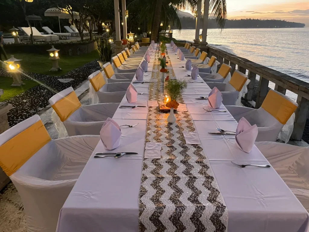 Long banquet table laid for dinner along the seafront terrace at dusk