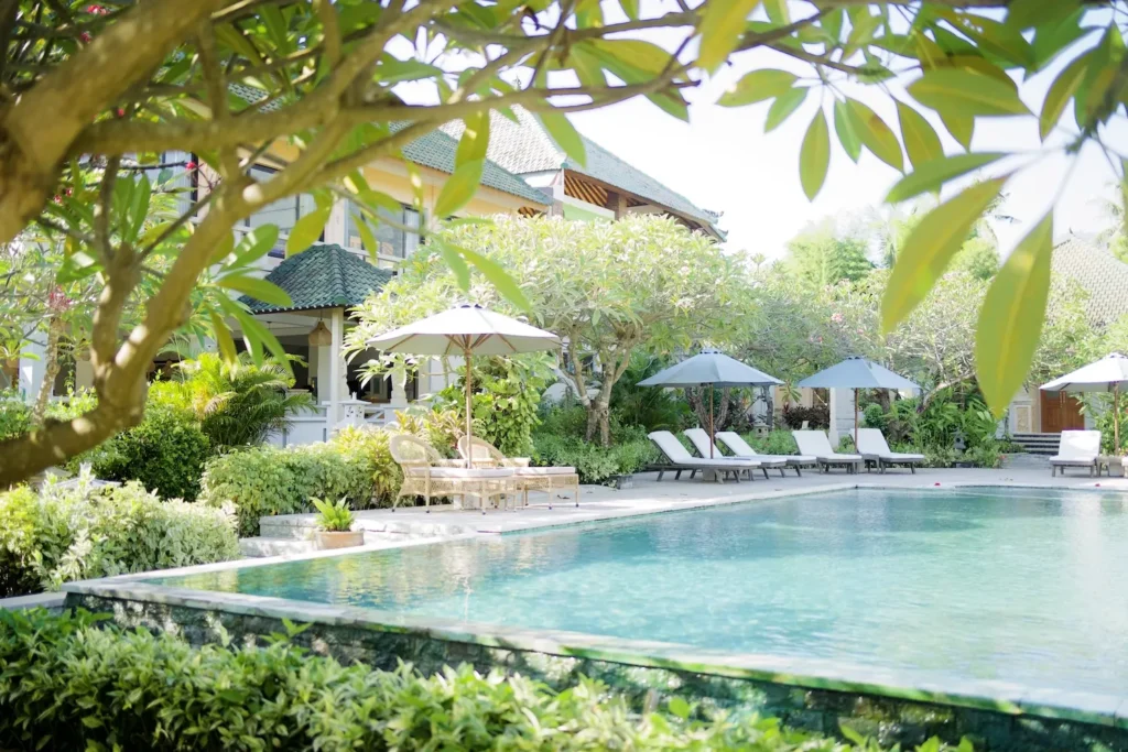 Poolside sun loungers under white parasols beside frangipani trees