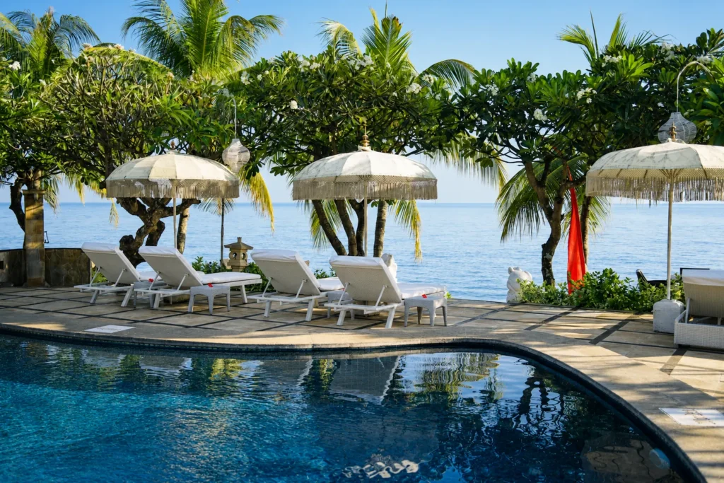 Swimming pool with white parasols, sun loungers and palm trees