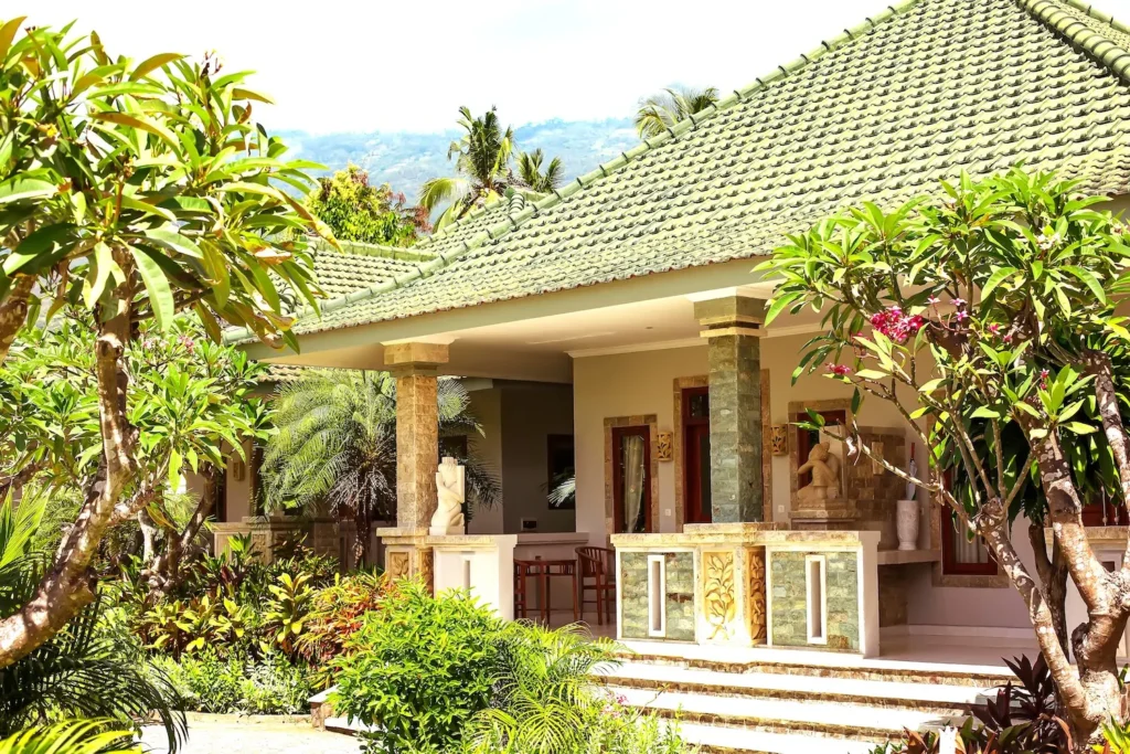 Villa exterior with a green tiled roof surrounded by lawn and frangipani trees
