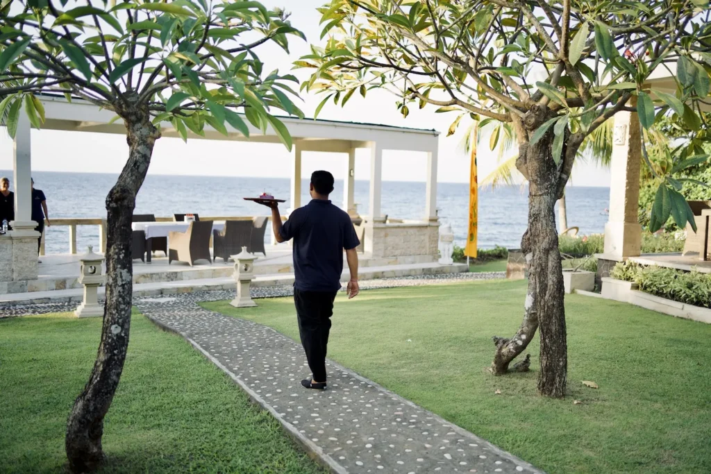 Waiter carrying a tray across the lawn toward the seafront dining pavilion