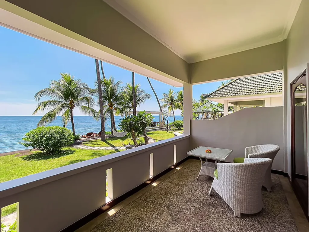 Covered villa terrace with wicker seating looking over the garden to the sea