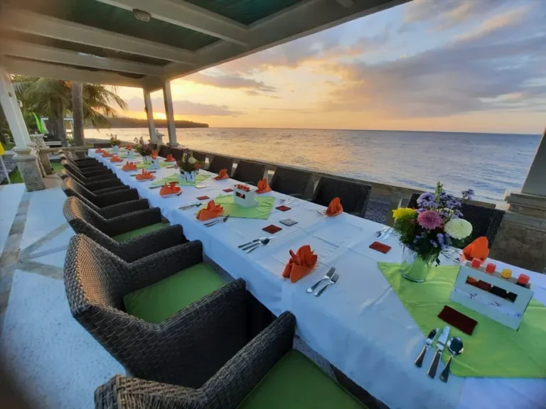 Long dinner table laid along the terrace with the sun setting over the sea