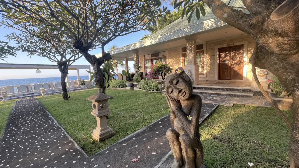 Carved stone figure on the lawn beneath a frangipani tree, villas behind