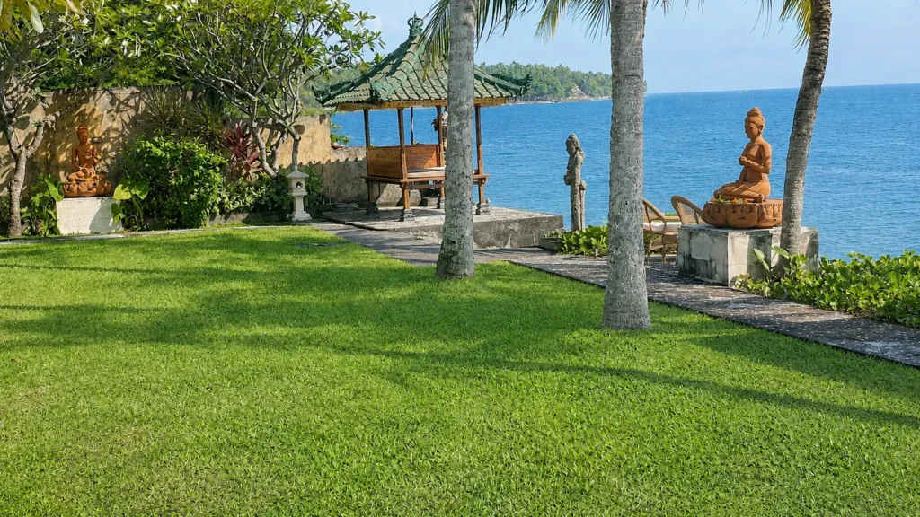 Wide lawn running to the sea wall, with a seated Buddha and palm trees